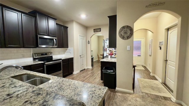 kitchen with sink, decorative backsplash, light stone counters, stainless steel appliances, and light wood-type flooring