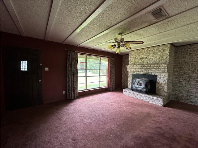 unfurnished living room with carpet, a wood stove, ceiling fan, a textured ceiling, and beamed ceiling