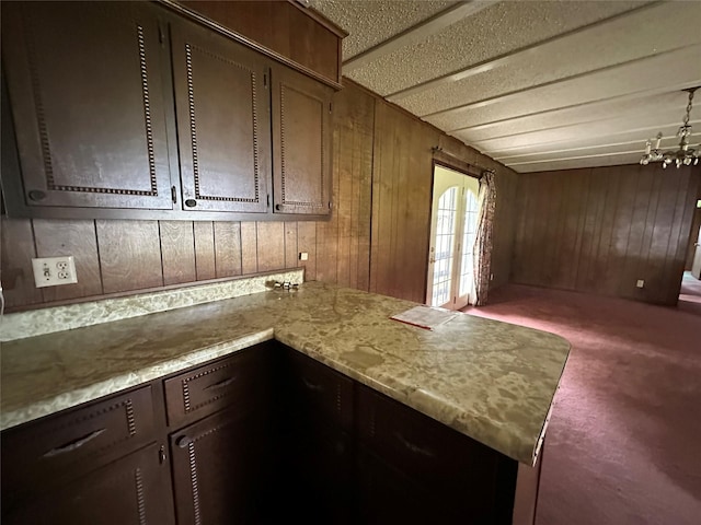 kitchen with dark colored carpet, dark brown cabinets, light stone counters, and wooden walls