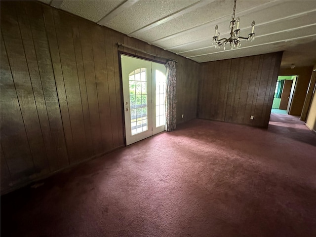 carpeted empty room featuring an inviting chandelier and wood walls