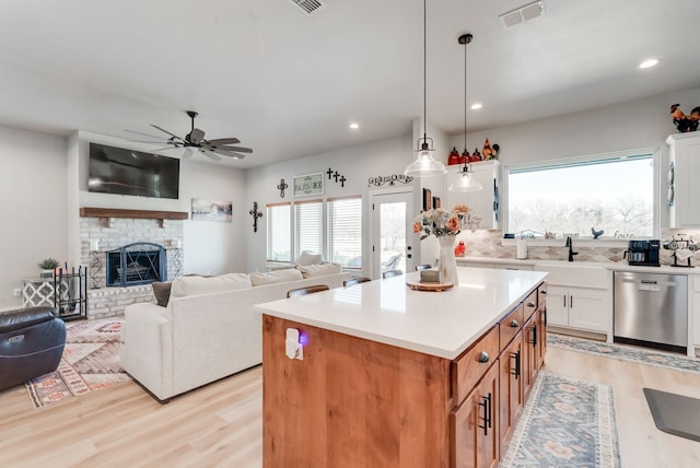 kitchen featuring a center island, dishwasher, hanging light fixtures, a brick fireplace, and white cabinets