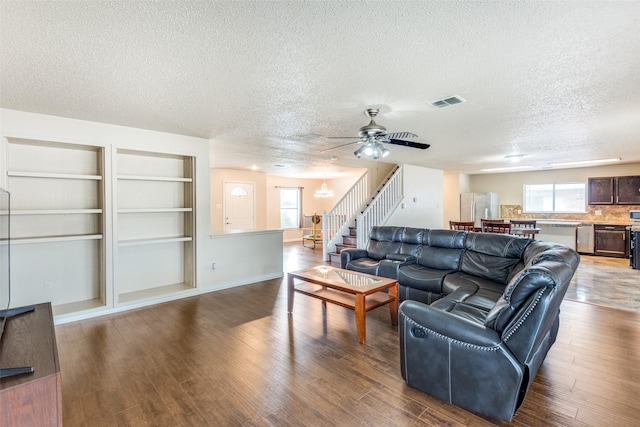 living room with wood-type flooring, ceiling fan with notable chandelier, a textured ceiling, and built in features