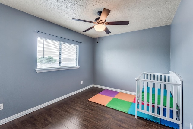 unfurnished bedroom featuring ceiling fan, dark hardwood / wood-style flooring, a crib, and a textured ceiling