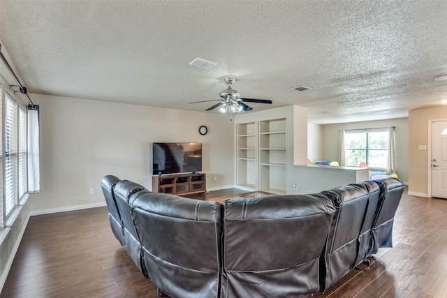 living room with built in shelves, ceiling fan, and dark wood-type flooring