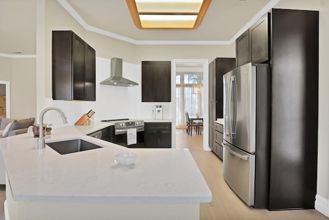 kitchen featuring dark brown cabinetry, sink, stainless steel appliances, wall chimney range hood, and ornamental molding