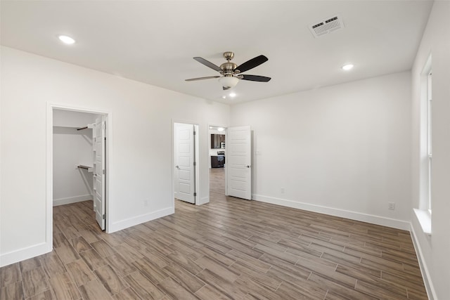 unfurnished bedroom featuring a spacious closet, a closet, ceiling fan, and light hardwood / wood-style flooring