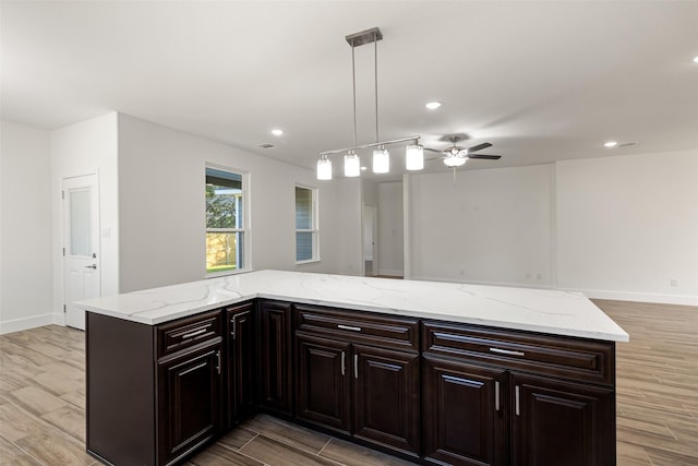 kitchen featuring light stone countertops, dark brown cabinetry, hanging light fixtures, and ceiling fan