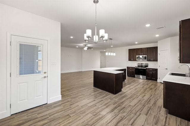 kitchen with dark brown cabinets, stainless steel appliances, sink, decorative light fixtures, and a kitchen island