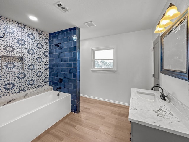 bathroom with vanity, a textured ceiling, wood-type flooring, and tiled shower / bath