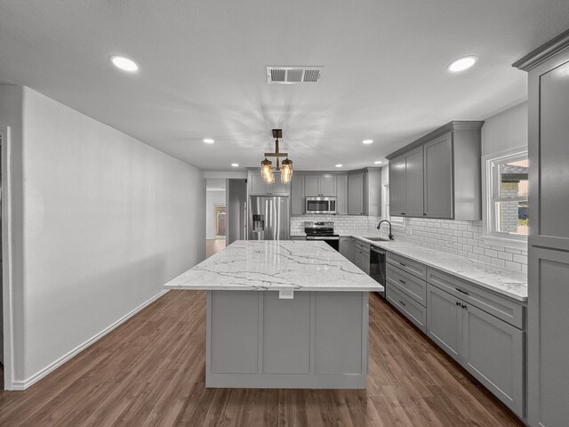 kitchen featuring a center island, stainless steel appliances, a barn door, decorative light fixtures, and gray cabinets