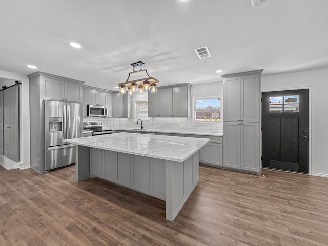 kitchen with appliances with stainless steel finishes, gray cabinets, a kitchen island, pendant lighting, and a barn door