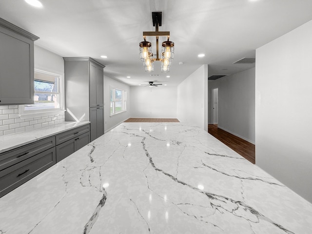 kitchen featuring tasteful backsplash, ceiling fan with notable chandelier, light stone counters, and gray cabinetry