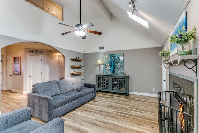 living room with high vaulted ceiling, a skylight, beamed ceiling, ceiling fan, and light hardwood / wood-style floors