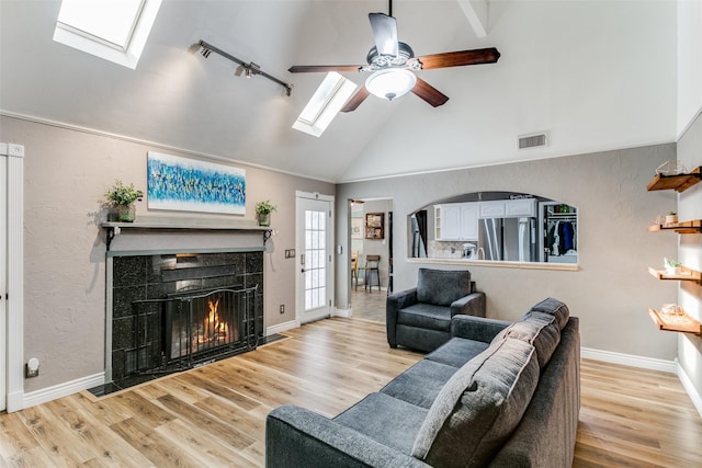 living room with a skylight, high vaulted ceiling, light wood-type flooring, ceiling fan, and a tiled fireplace