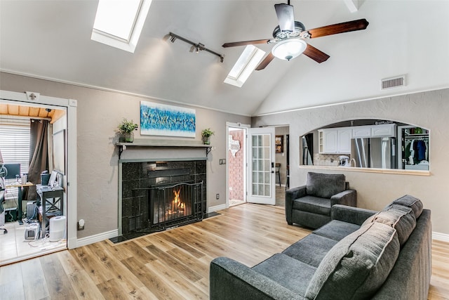 living room with a tile fireplace, ceiling fan, light hardwood / wood-style floors, and a skylight