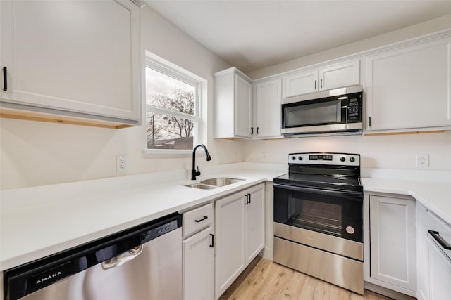 kitchen with appliances with stainless steel finishes, sink, white cabinets, and light hardwood / wood-style flooring