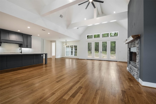 unfurnished living room with dark hardwood / wood-style flooring, ceiling fan with notable chandelier, high vaulted ceiling, beamed ceiling, and a fireplace