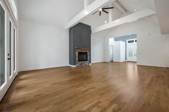 unfurnished living room featuring ceiling fan, wood-type flooring, high vaulted ceiling, beamed ceiling, and a fireplace