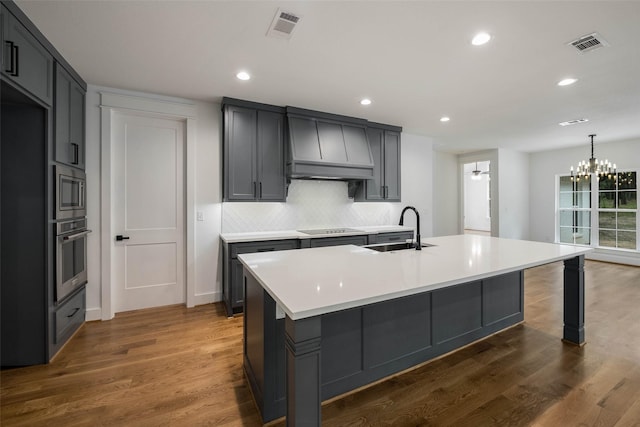 kitchen with a center island with sink, sink, appliances with stainless steel finishes, a notable chandelier, and dark hardwood / wood-style flooring