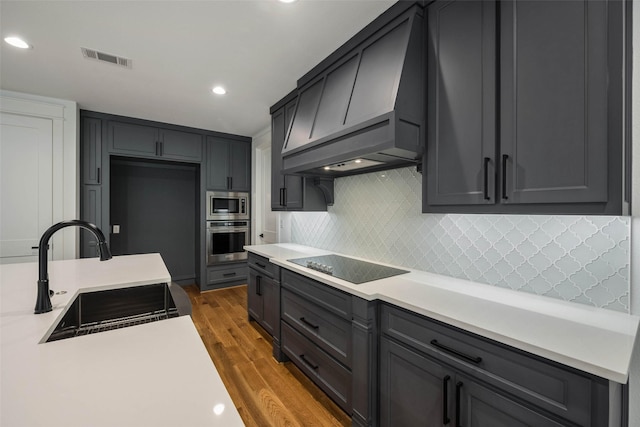 kitchen with appliances with stainless steel finishes, tasteful backsplash, custom range hood, sink, and light hardwood / wood-style flooring