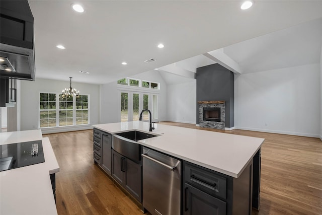 kitchen with dishwasher, a center island with sink, a stone fireplace, sink, and a notable chandelier