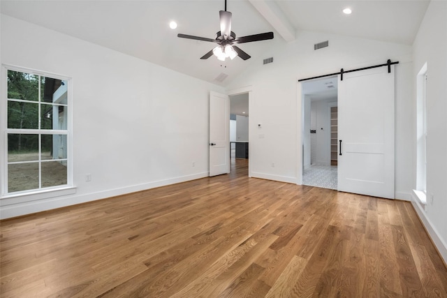 unfurnished bedroom featuring a barn door, ceiling fan, lofted ceiling with beams, and light wood-type flooring