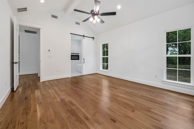 unfurnished bedroom with ceiling fan, wood-type flooring, a barn door, lofted ceiling with beams, and multiple windows