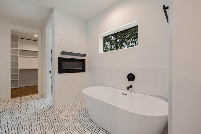 bathroom with tile walls, a bath, tile patterned flooring, and a large fireplace