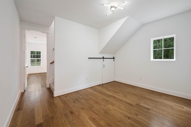 additional living space featuring a barn door, hardwood / wood-style floors, and vaulted ceiling