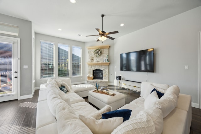 living room featuring dark hardwood / wood-style flooring, a stone fireplace, and ceiling fan