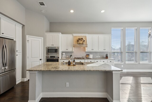 kitchen with white cabinetry, light stone counters, a center island with sink, stainless steel appliances, and decorative backsplash