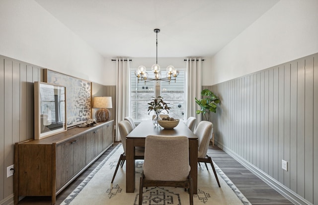 dining area with wooden walls, wood-type flooring, and a notable chandelier