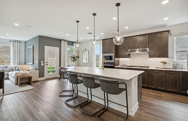 kitchen with a breakfast bar, dark hardwood / wood-style flooring, decorative light fixtures, and a kitchen island with sink