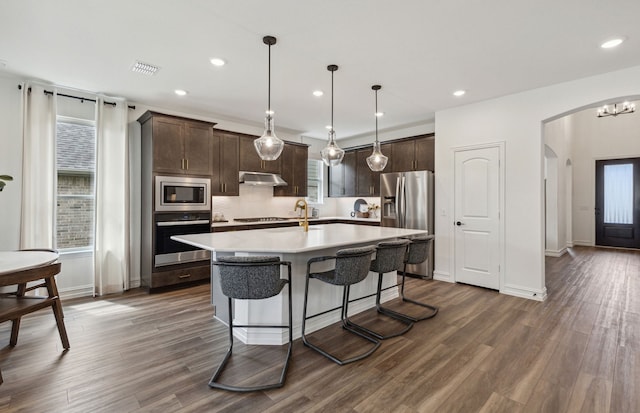 kitchen featuring stainless steel appliances, dark hardwood / wood-style floors, pendant lighting, a kitchen island with sink, and dark brown cabinets