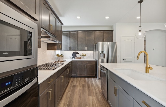 kitchen with sink, stainless steel appliances, tasteful backsplash, range hood, and decorative light fixtures