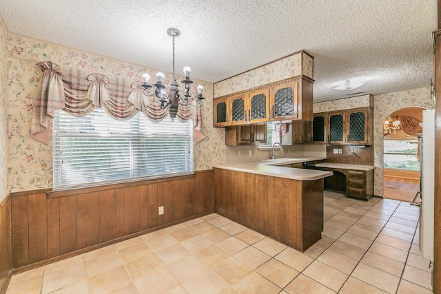 kitchen with sink, an inviting chandelier, hanging light fixtures, a textured ceiling, and kitchen peninsula