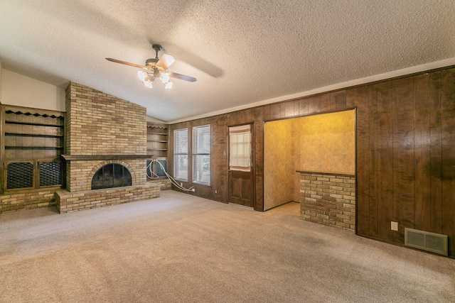 unfurnished living room featuring lofted ceiling, wooden walls, a textured ceiling, light carpet, and a brick fireplace