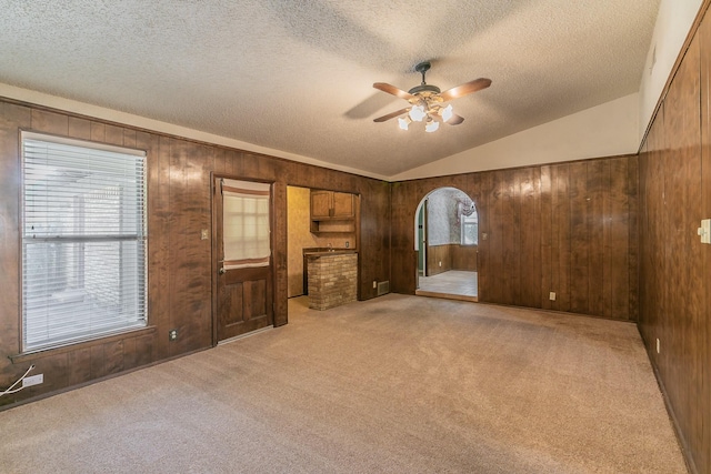 carpeted spare room with vaulted ceiling, a textured ceiling, ceiling fan, and wood walls