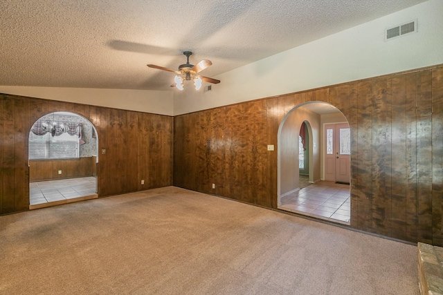 carpeted empty room featuring lofted ceiling, a textured ceiling, ceiling fan, and wood walls