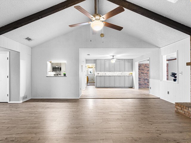 unfurnished living room with ceiling fan, a brick fireplace, vaulted ceiling with beams, dark hardwood / wood-style flooring, and a textured ceiling