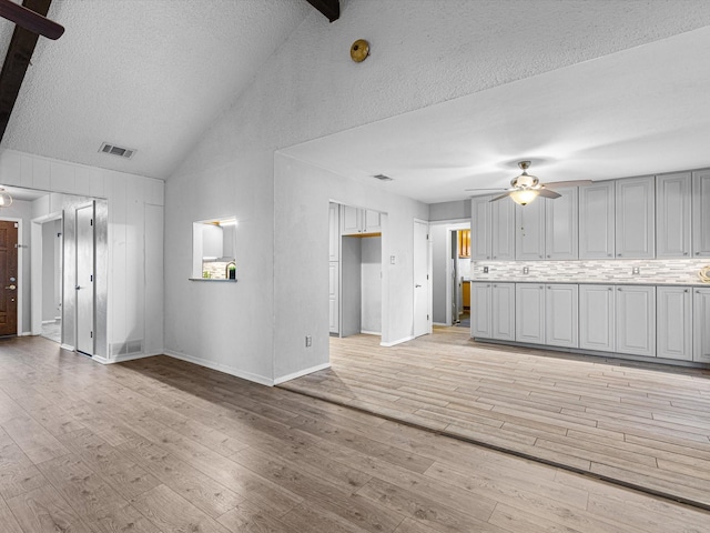 unfurnished living room with a textured ceiling, vaulted ceiling, light hardwood / wood-style flooring, and ceiling fan