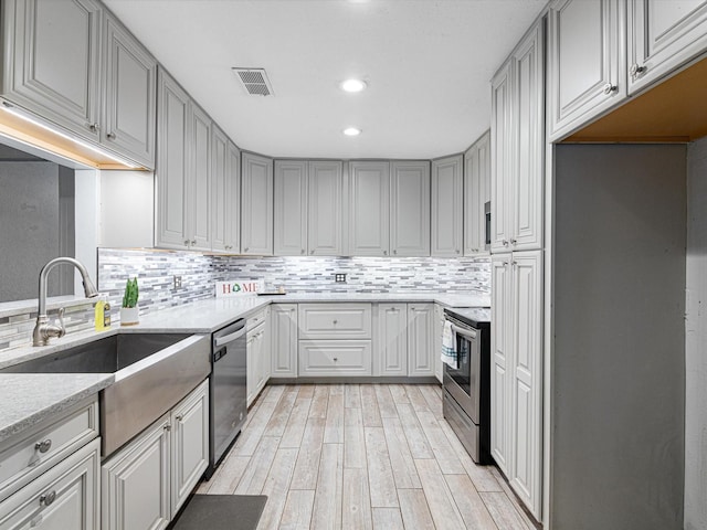 kitchen with gray cabinets, sink, backsplash, stainless steel appliances, and light hardwood / wood-style flooring