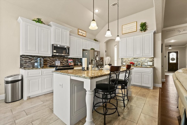 kitchen with an island with sink, white cabinets, dark stone counters, and appliances with stainless steel finishes