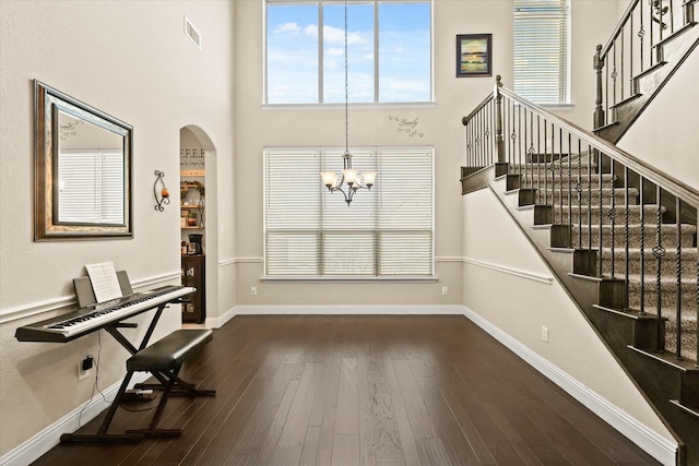 entryway with a towering ceiling, dark wood-type flooring, and an inviting chandelier