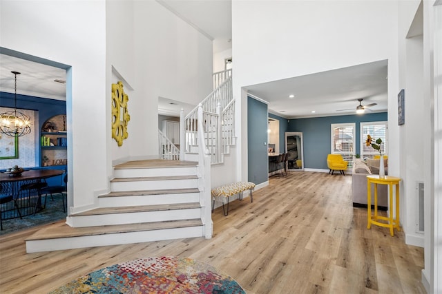 entryway with crown molding, light hardwood / wood-style floors, and ceiling fan with notable chandelier