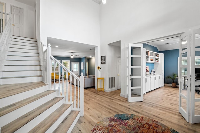 staircase with ceiling fan, wood-type flooring, crown molding, and a towering ceiling