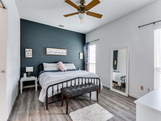 bedroom featuring hardwood / wood-style flooring, ceiling fan, wood walls, and a textured ceiling