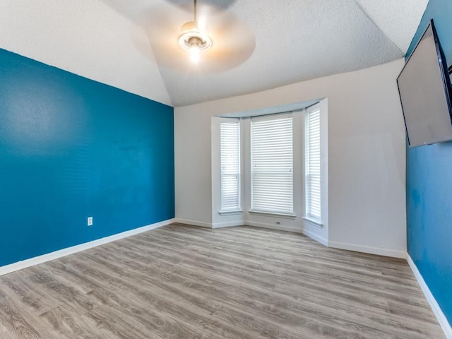 empty room with light wood-type flooring, vaulted ceiling, a wealth of natural light, and ceiling fan