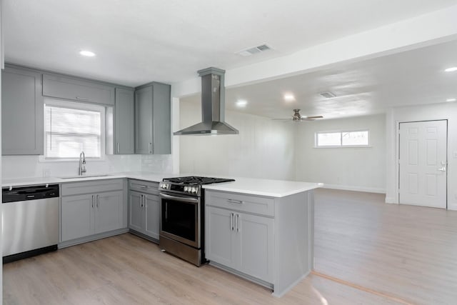 kitchen with sink, wall chimney exhaust hood, ceiling fan, light hardwood / wood-style floors, and stainless steel appliances