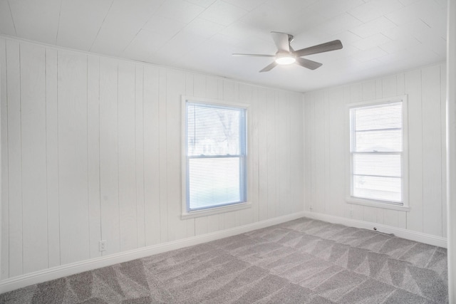 carpeted spare room featuring ceiling fan and wood walls